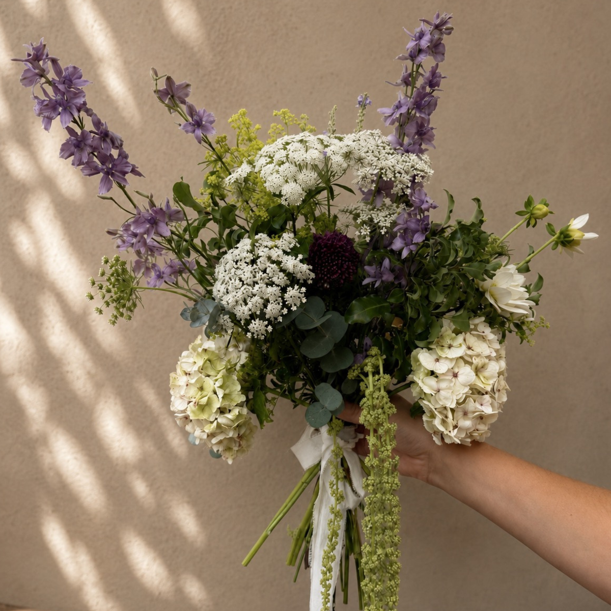 Hand-tied bouquet with white hydrangeas, purple delphiniums and trailing green amaranthus.