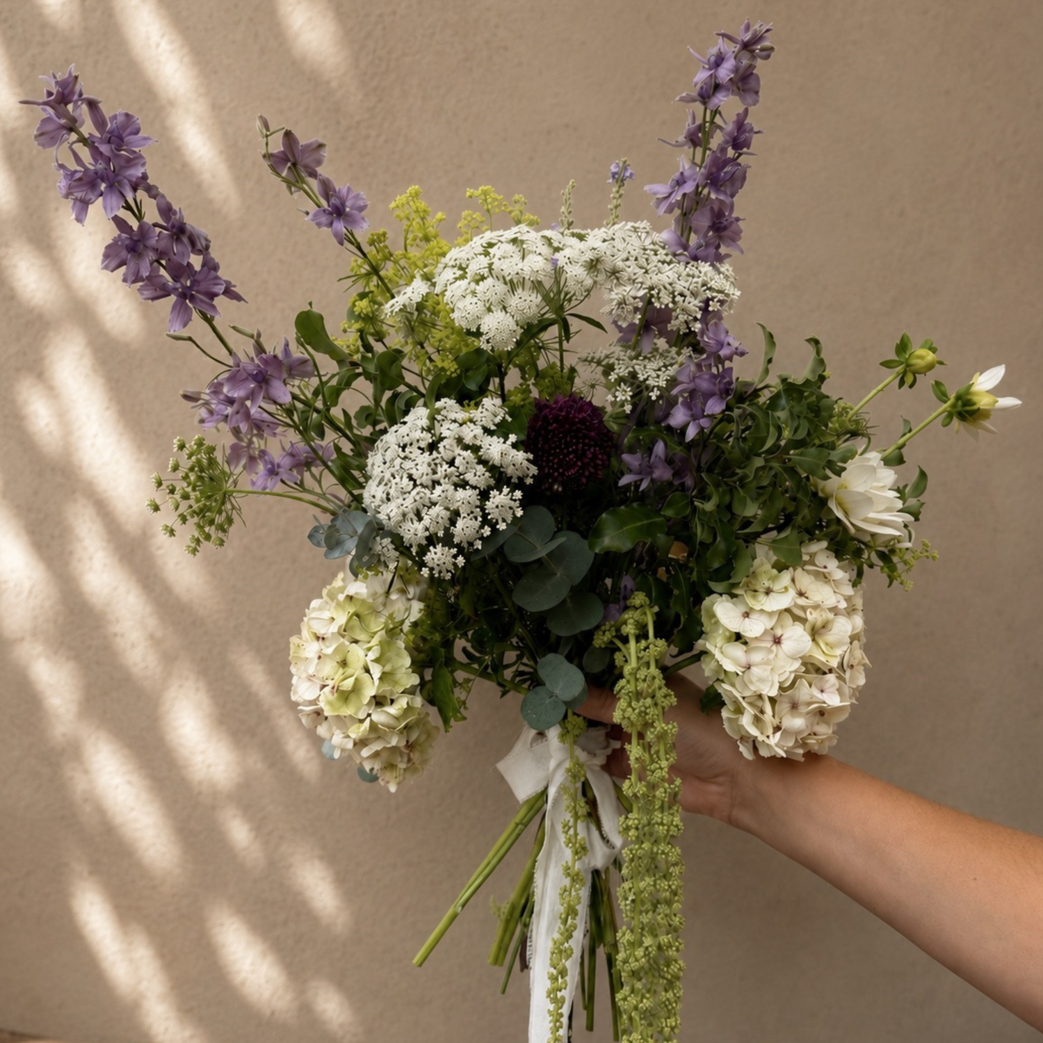 Hand-tied bouquet with white hydrangeas, purple delphiniums and trailing green amaranthus.